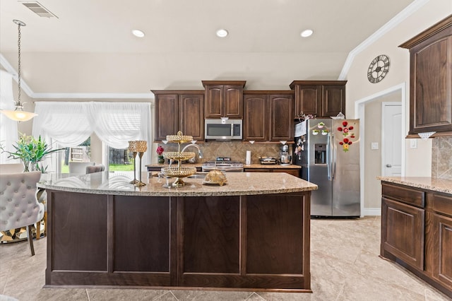 kitchen featuring dark brown cabinetry, light stone countertops, decorative light fixtures, a kitchen island with sink, and appliances with stainless steel finishes