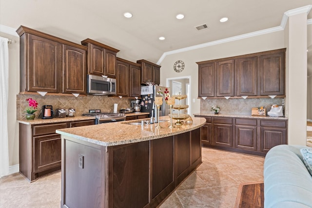 kitchen with decorative backsplash, appliances with stainless steel finishes, dark brown cabinetry, and a center island with sink