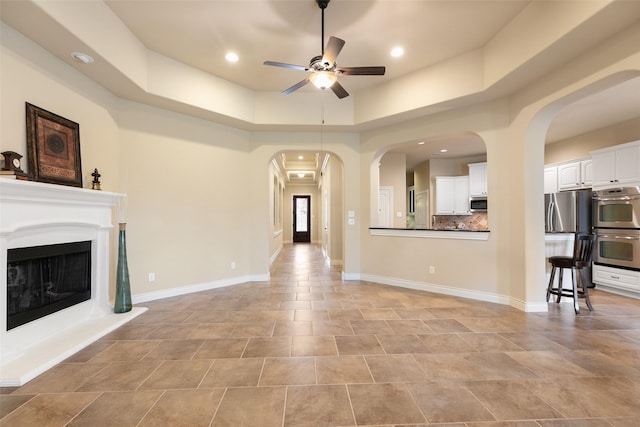 unfurnished living room with a raised ceiling and ceiling fan