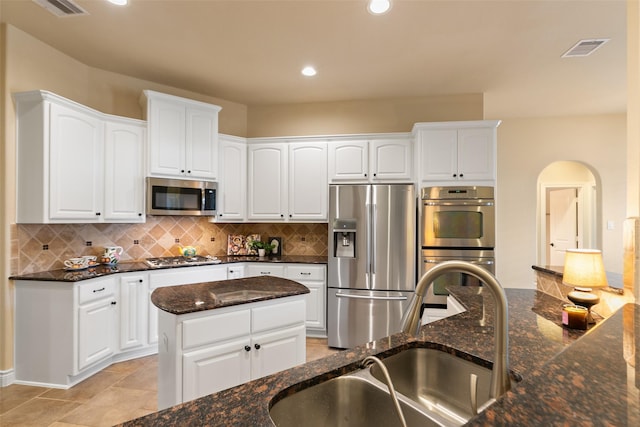 kitchen with sink, stainless steel appliances, tasteful backsplash, dark stone countertops, and white cabinets