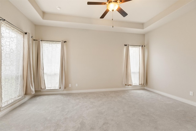 unfurnished room featuring ceiling fan, a healthy amount of sunlight, and a tray ceiling