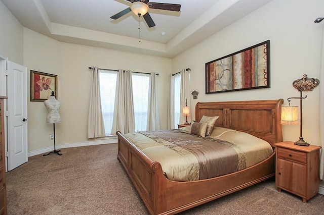 carpeted bedroom with a raised ceiling and ceiling fan