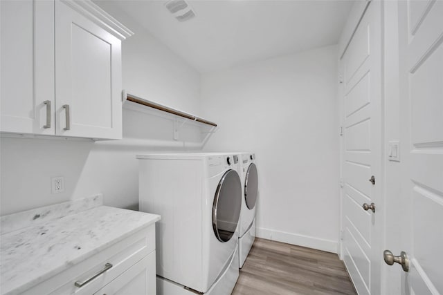 laundry area with washing machine and dryer, cabinets, and light hardwood / wood-style floors