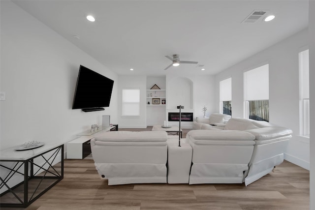 living room with built in shelves, ceiling fan, and light hardwood / wood-style floors