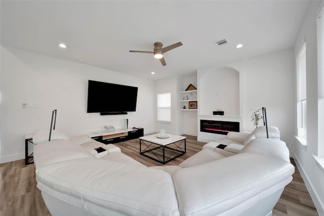 living room with ceiling fan, built in features, and wood-type flooring