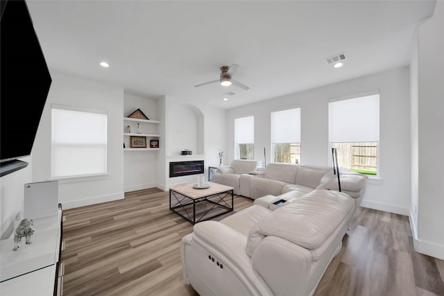 living room with built in shelves, light hardwood / wood-style flooring, and ceiling fan