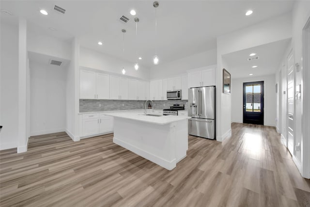 kitchen featuring sink, hanging light fixtures, a center island with sink, appliances with stainless steel finishes, and light wood-type flooring