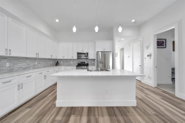 kitchen featuring a center island with sink, white cabinetry, stainless steel appliances, and light hardwood / wood-style flooring