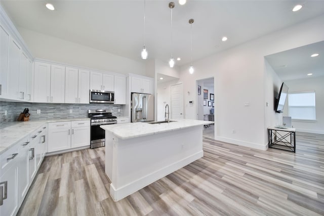 kitchen with white cabinets, a center island with sink, light stone countertops, light wood-type flooring, and stainless steel appliances