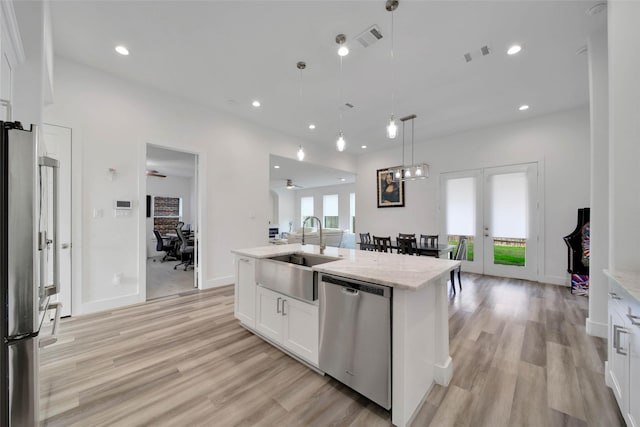 kitchen with appliances with stainless steel finishes, sink, pendant lighting, white cabinetry, and an island with sink