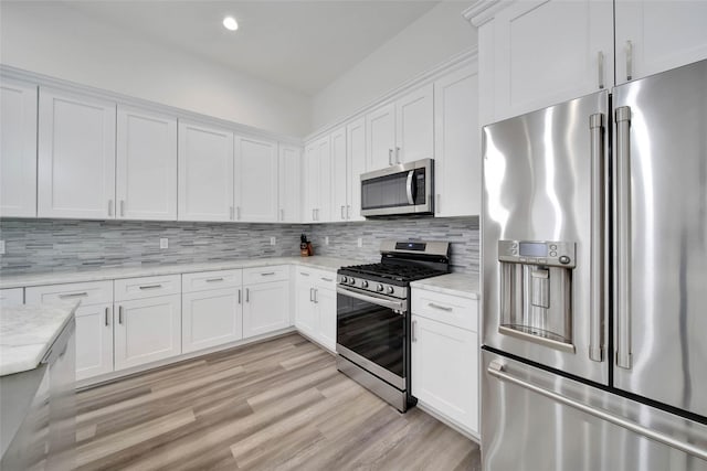 kitchen with white cabinets, decorative backsplash, light wood-type flooring, light stone countertops, and stainless steel appliances