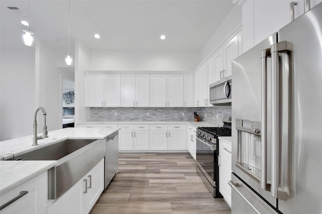 kitchen with white cabinets, light hardwood / wood-style floors, light stone countertops, and stainless steel appliances