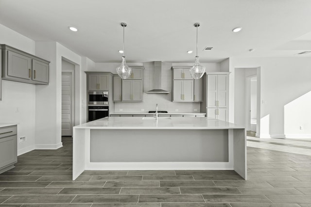 kitchen with a spacious island, wall chimney exhaust hood, gray cabinets, decorative light fixtures, and dark hardwood / wood-style flooring