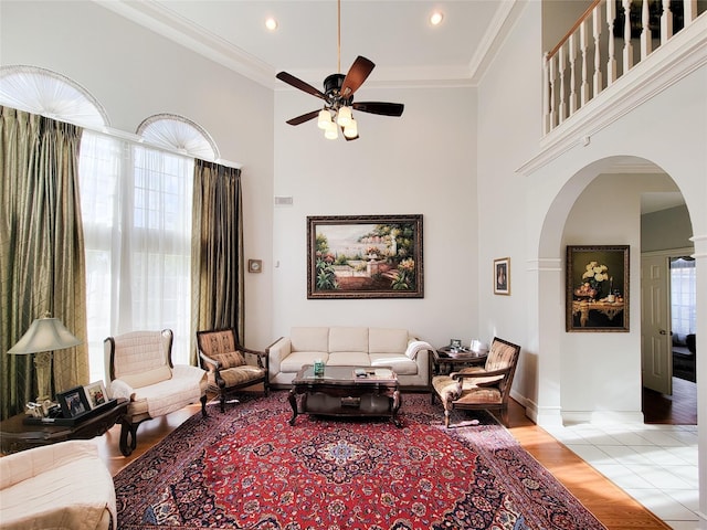 living room with ceiling fan, a towering ceiling, ornamental molding, and light hardwood / wood-style flooring