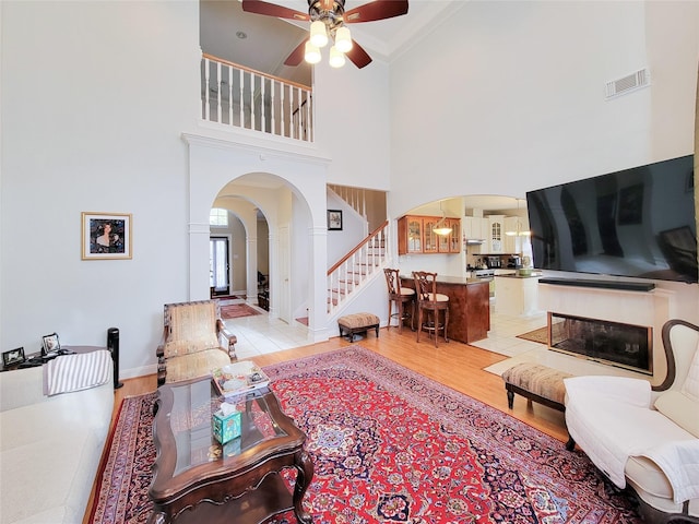 living room featuring ceiling fan, a towering ceiling, ornamental molding, and light wood-type flooring