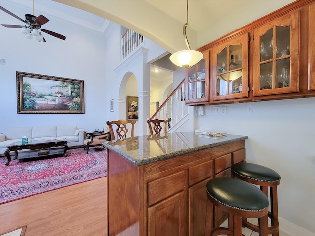 interior space with hanging light fixtures, light hardwood / wood-style flooring, ceiling fan, dark stone countertops, and ornamental molding