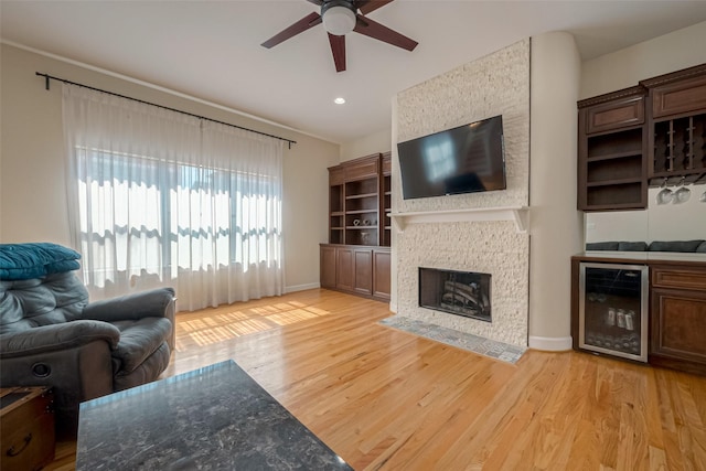 living room with a fireplace, light wood-type flooring, beverage cooler, and ceiling fan