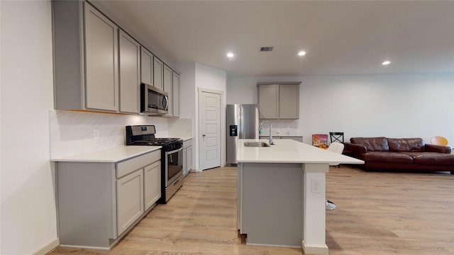 kitchen with gray cabinets, light hardwood / wood-style floors, backsplash, and appliances with stainless steel finishes