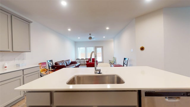 kitchen with tasteful backsplash, stainless steel dishwasher, gray cabinetry, sink, and light hardwood / wood-style flooring