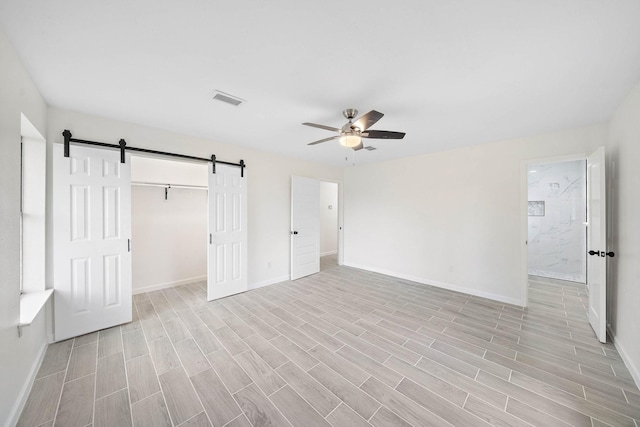 unfurnished bedroom with light wood-type flooring, a closet, ceiling fan, and a barn door