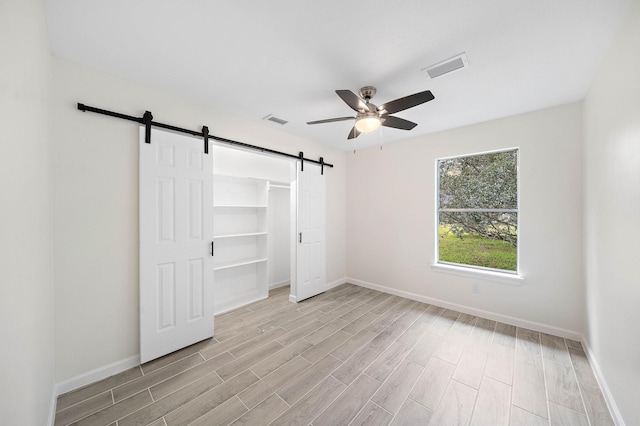 unfurnished bedroom with ceiling fan, a barn door, a closet, and light hardwood / wood-style flooring