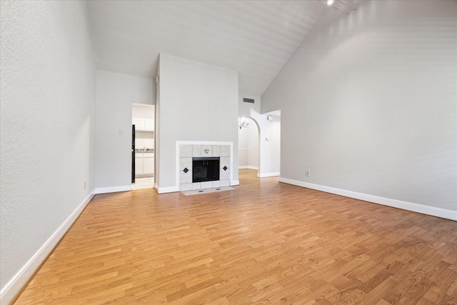 unfurnished living room featuring a fireplace, high vaulted ceiling, and light hardwood / wood-style floors