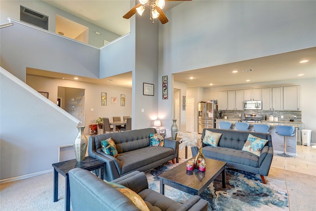 living room with ceiling fan, light colored carpet, and a towering ceiling