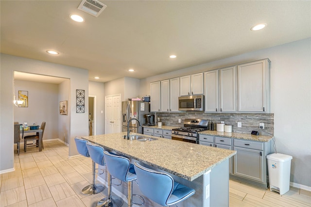 kitchen featuring a breakfast bar, appliances with stainless steel finishes, light stone countertops, and gray cabinetry