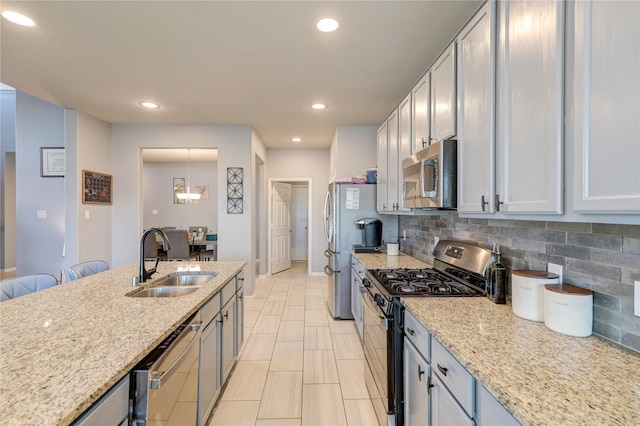 kitchen featuring sink, light stone countertops, appliances with stainless steel finishes, tasteful backsplash, and decorative light fixtures