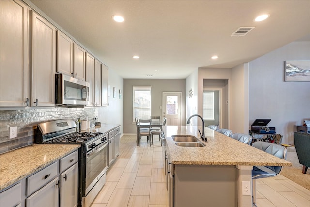 kitchen with a breakfast bar, a center island with sink, sink, appliances with stainless steel finishes, and light stone counters