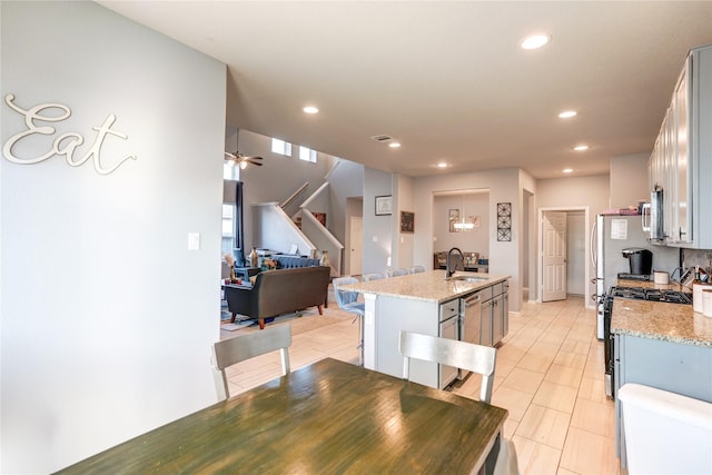 kitchen with sink, gas range, an island with sink, light stone counters, and white cabinetry