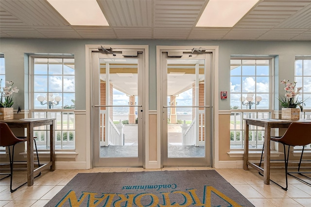 doorway with light tile patterned floors, a paneled ceiling, and plenty of natural light