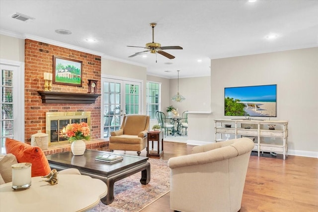 living room featuring a fireplace, light wood-type flooring, ceiling fan, and crown molding