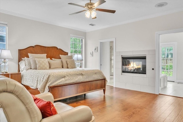 bedroom featuring hardwood / wood-style floors, a tiled fireplace, multiple windows, and ceiling fan