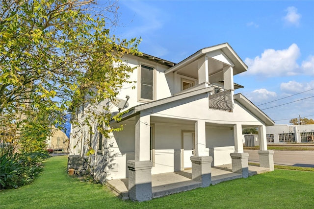 view of side of home with a porch, a balcony, and a lawn