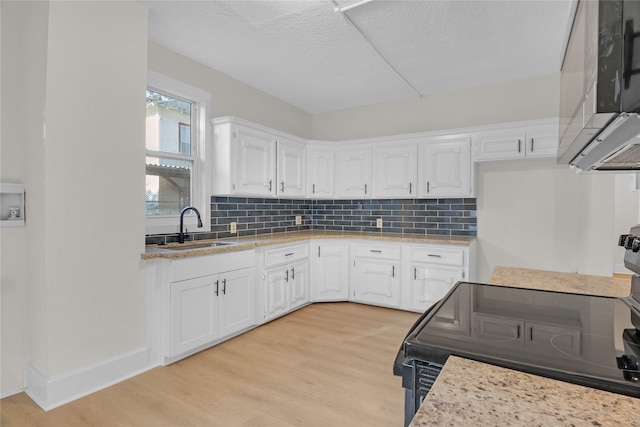 kitchen with light stone countertops, white cabinetry, sink, and light hardwood / wood-style floors