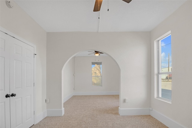 empty room featuring light colored carpet, ceiling fan, and a healthy amount of sunlight