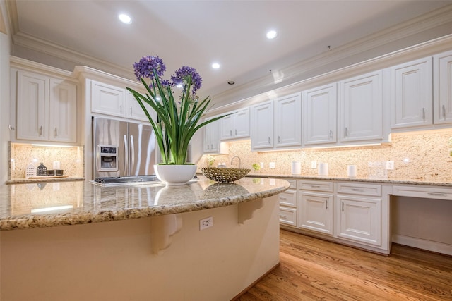 kitchen with light stone countertops, stainless steel fridge, crown molding, white cabinets, and light hardwood / wood-style floors