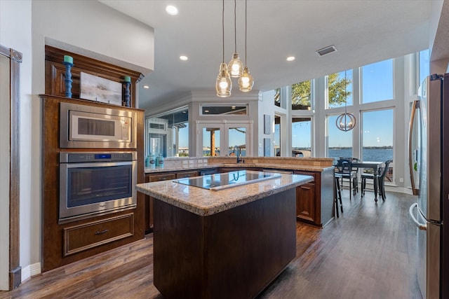 kitchen featuring stainless steel appliances, decorative light fixtures, a water view, a chandelier, and a kitchen island