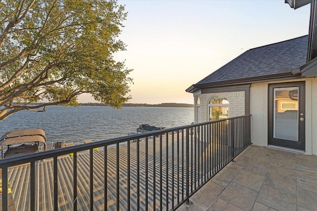 balcony at dusk featuring a water view