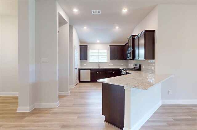 19818 Paros Island Dr, Hockley, TX 77447 - kitchen with stainless steel appliances, dark brown cabinetry, light wood-type flooring, decorative backsplash, and a peninsula
