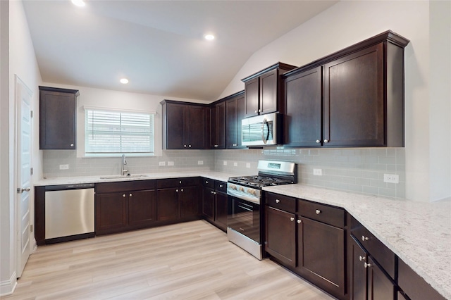 19818 Paros Island Dr, Hockley, TX 77447 - kitchen with stainless steel appliances, vaulted ceiling, dark brown cabinets, light stone counters, and light wood-style floors