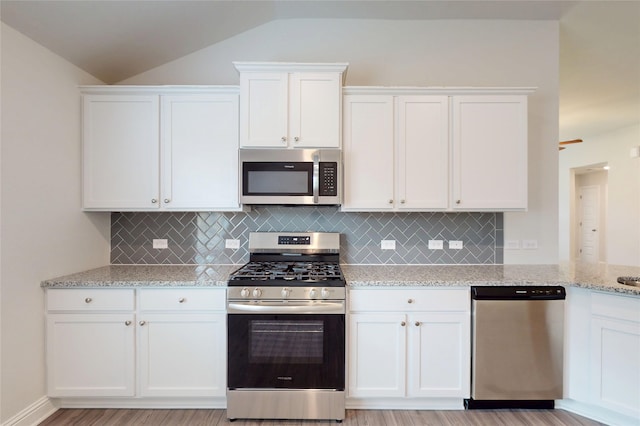 19814 Paros Island Dr, Hockley, TX 77447 - kitchen featuring appliances with stainless steel finishes, white cabinetry, lofted ceiling, backsplash, and light stone countertops
