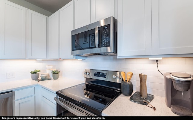 kitchen with stainless steel appliances, white cabinetry, tasteful backsplash, and light stone counters