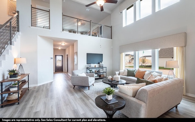 living room featuring ceiling fan, a towering ceiling, a healthy amount of sunlight, and light wood-type flooring