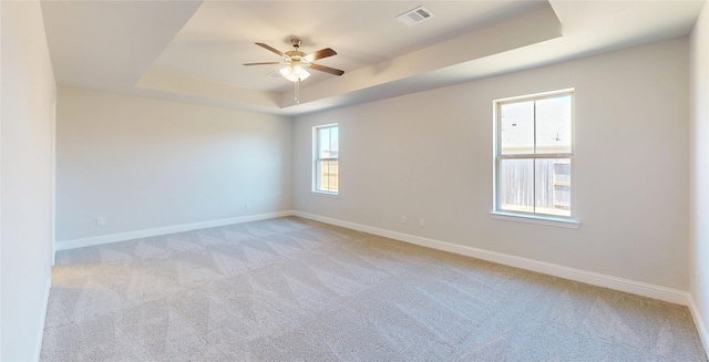 spare room with light colored carpet, a tray ceiling, visible vents, and baseboards