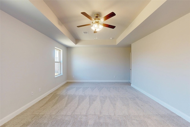 spare room with light carpet, baseboards, visible vents, a raised ceiling, and ceiling fan