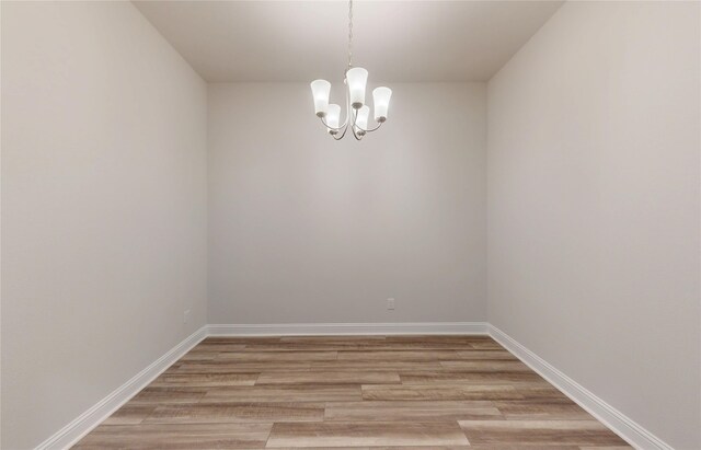 spare room with light wood-type flooring, baseboards, and an inviting chandelier