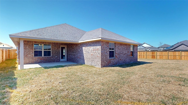 rear view of property with brick siding, roof with shingles, a lawn, a patio area, and a fenced backyard