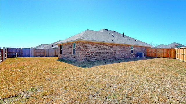 back of house with a fenced backyard, central air condition unit, brick siding, a shingled roof, and a yard